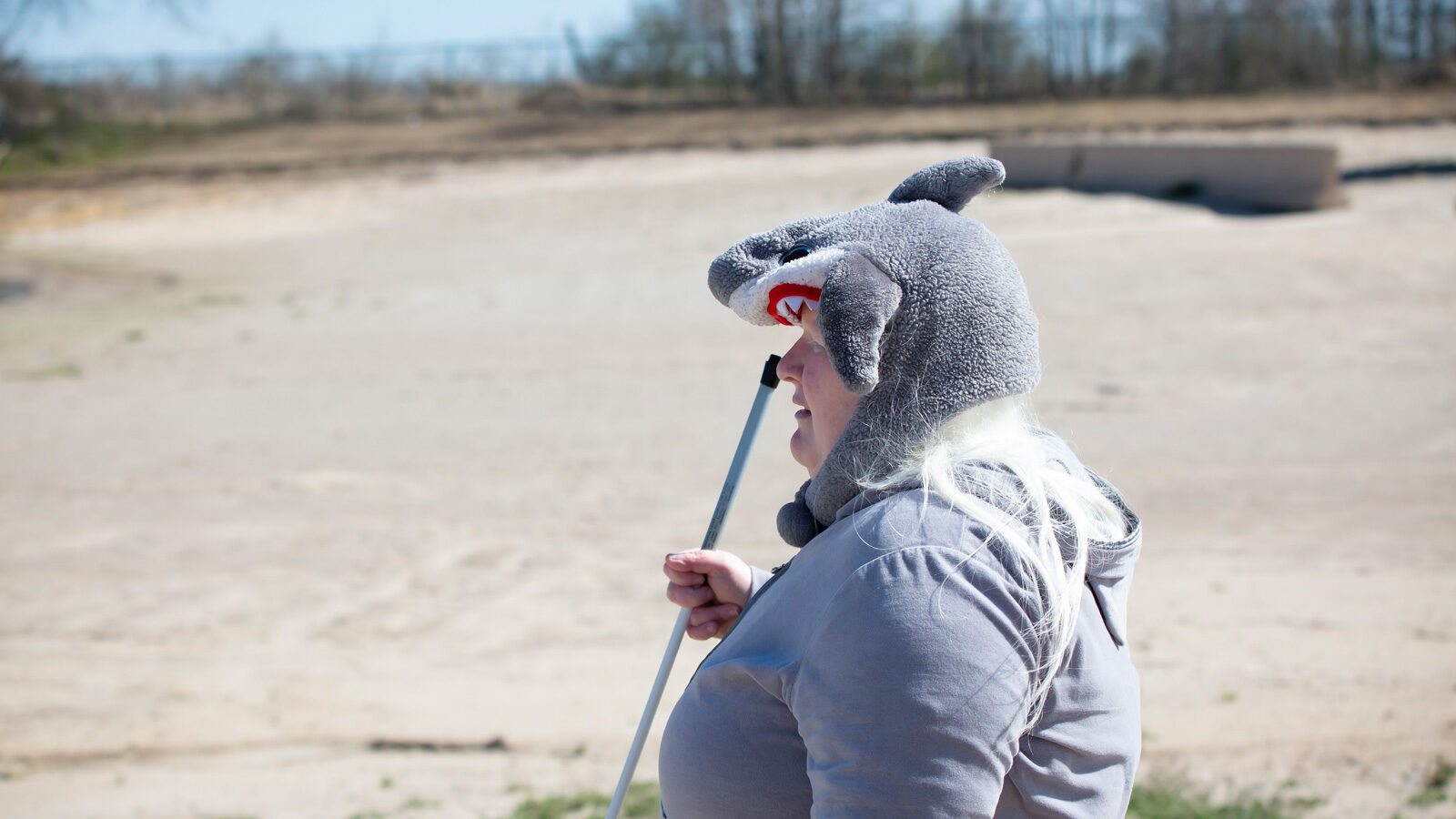 Ginny standing on an empty beach with her cane and shark hat